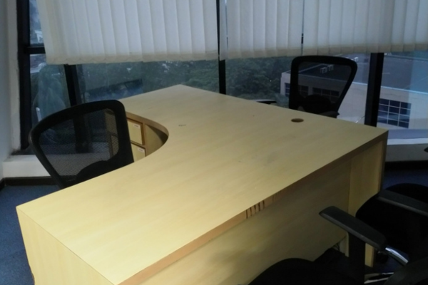 A well-lit private office cabin at Infinity Business Centre with an L-shaped corner desk and a window view, offering a quiet, dedicated workspace for executives and business owners.