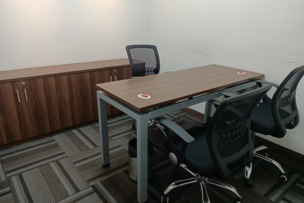 A small, modern co-working office space with a wooden desk, three mesh chairs, and a matching wooden storage cabinet.